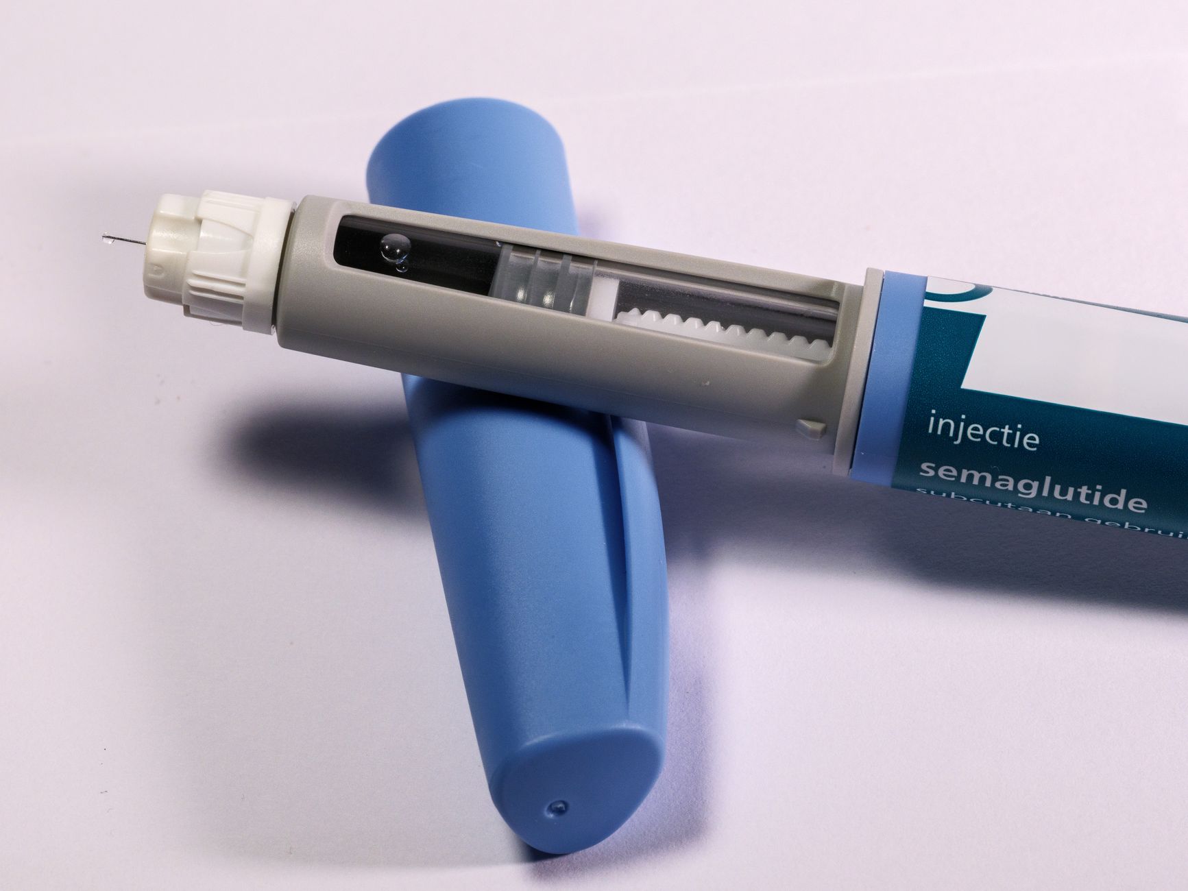 Stylo injecteur de sémaglutide avec aiguille apparente, posé sur son capuchon bleu sur fond clair